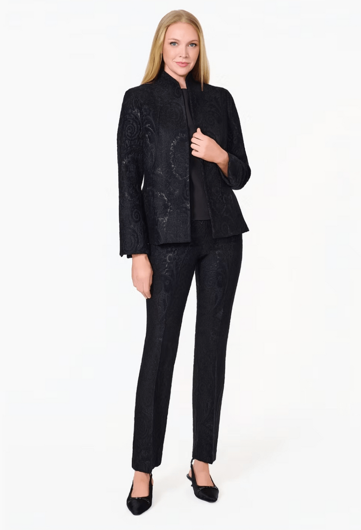 A woman modeling a black two-piece suit with a subtle tonal damask pattern, featuring a cropped jacket with a stand collar and matching slim trousers, against a plain white studio background.