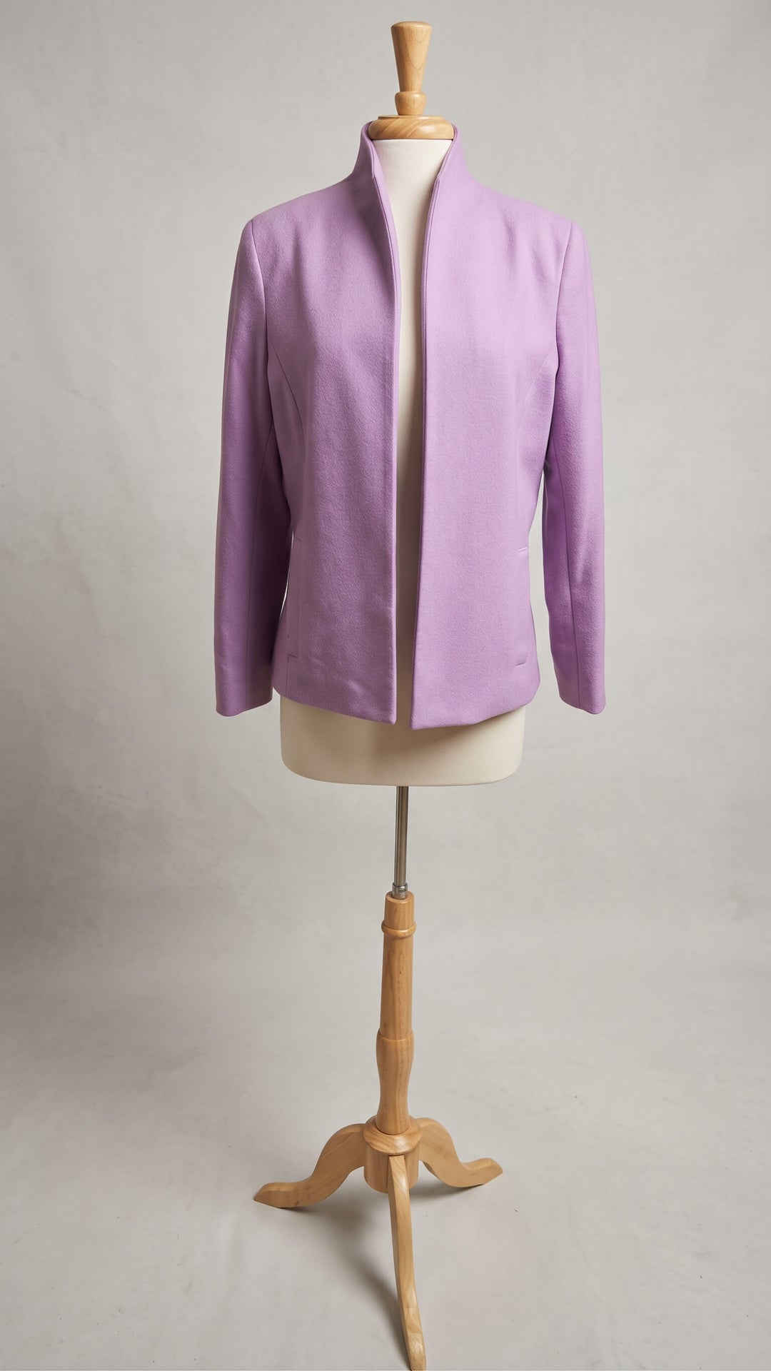 A lavender purple jacket displayed on a cream-colored dress form mannequin mounted on a wooden stand, set against a neutral light gray background.