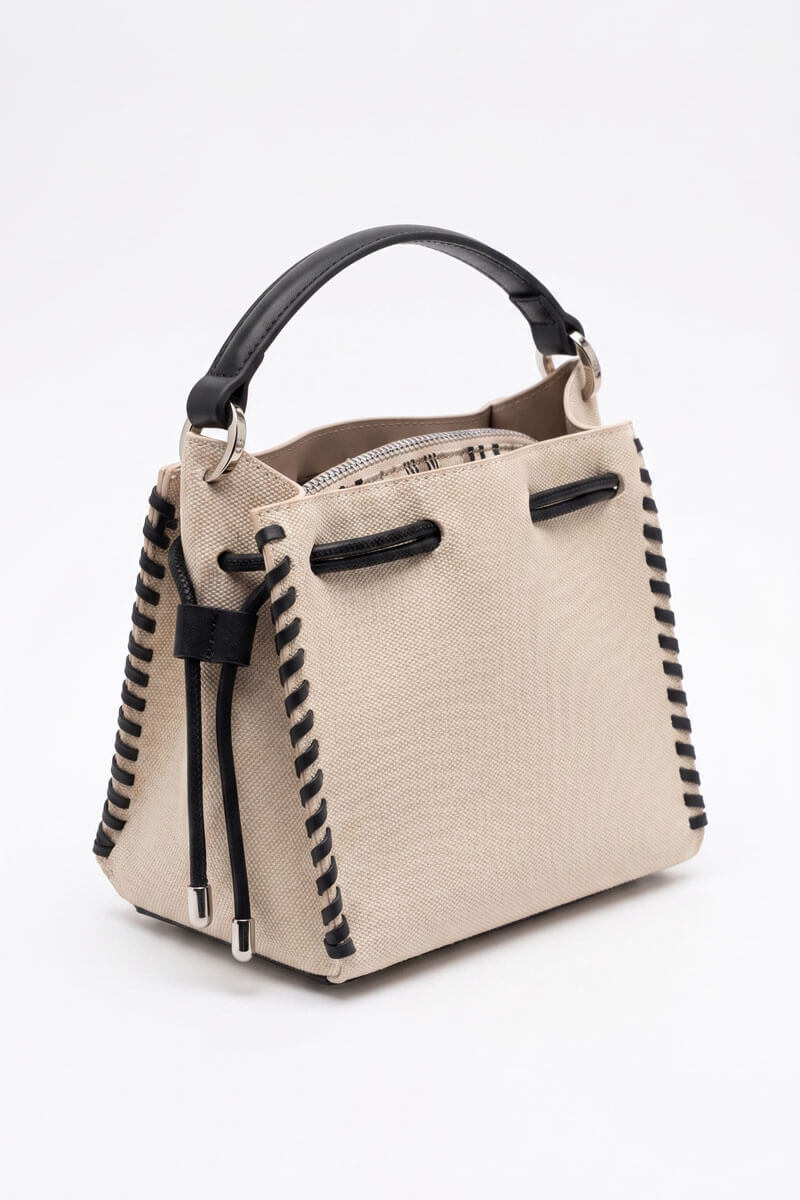 A structured beige canvas handbag with black trim, a black top handle, and black braided rope details along the sides and hanging from the top, shown on a plain white background.