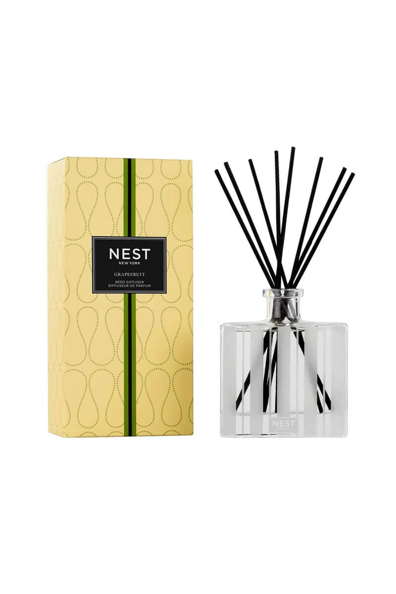 A reed diffuser bottle with black reeds next to its yellow patterned packaging box, both featuring the NEST brand label, on a solid white background.