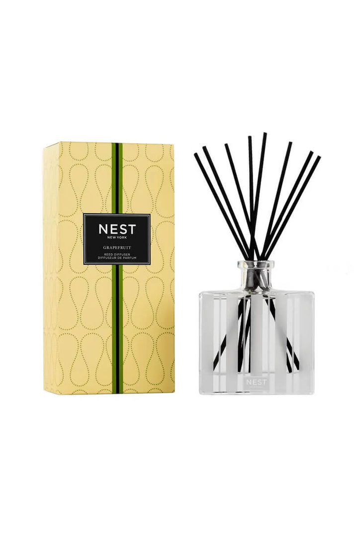 A reed diffuser bottle with black reeds next to its yellow patterned packaging box, both featuring the NEST brand label, on a solid white background.