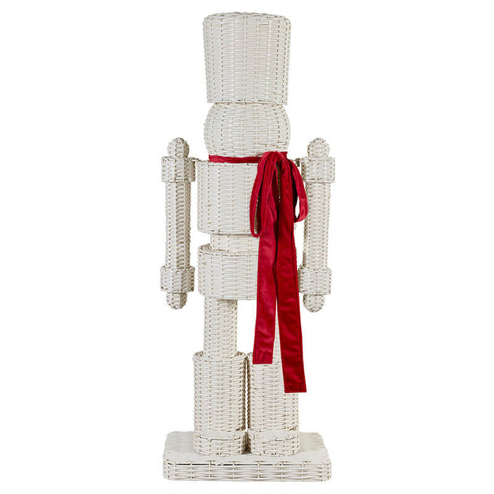 A white wicker-style nutcracker decoration with a bright red velvet ribbon tied around the waist, shown against a plain white background.